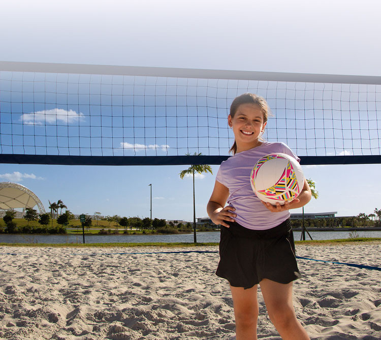 A girl smiling while holding a volleyball on the beach.