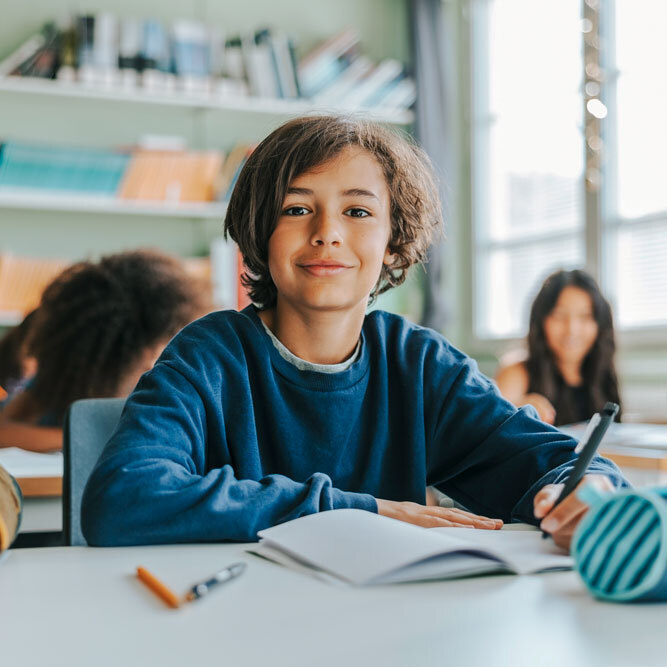 A boy smiling at his desk in a classroom.