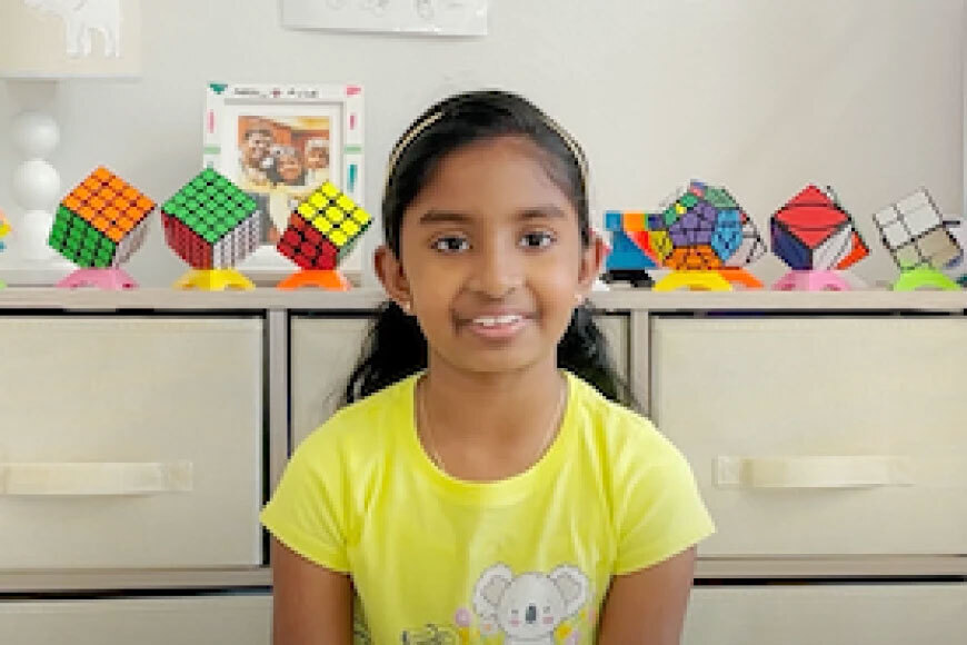 Photograph of a girl smiling in front of a collection of Rubik's Cubes.