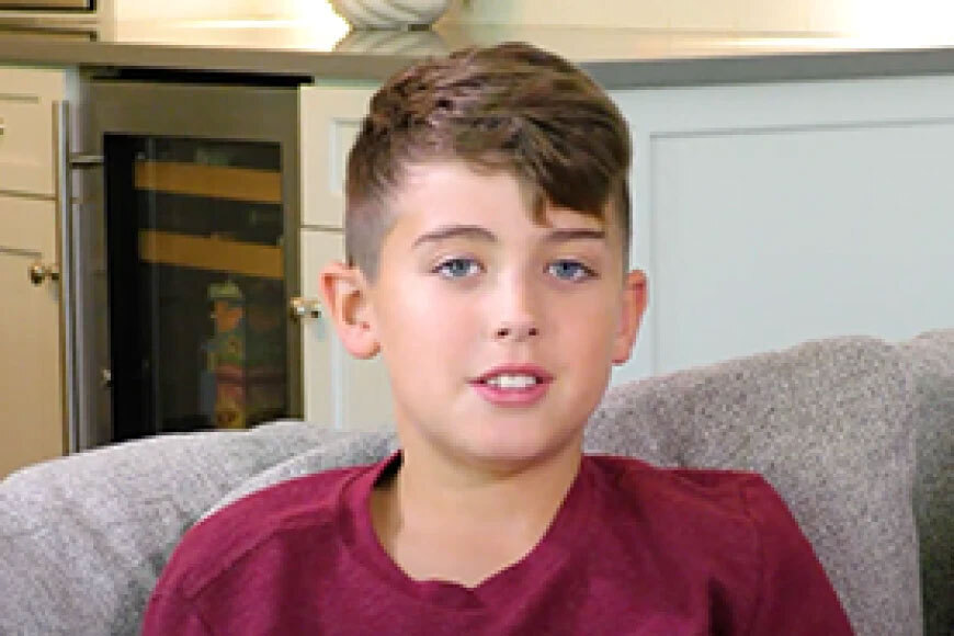 Photograph of a boy smiling and sitting on a couch.