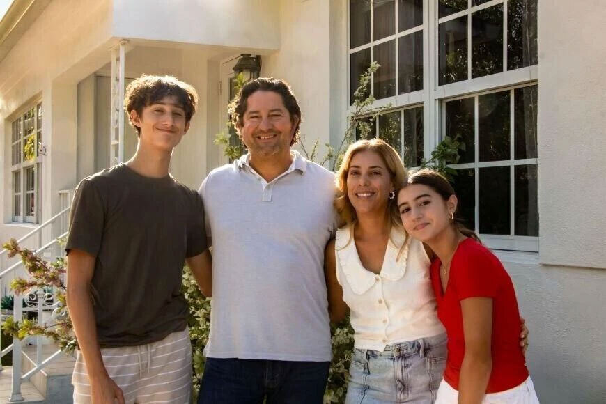 Photograph of a mother, father, son, and daughter smiling in front of their house.