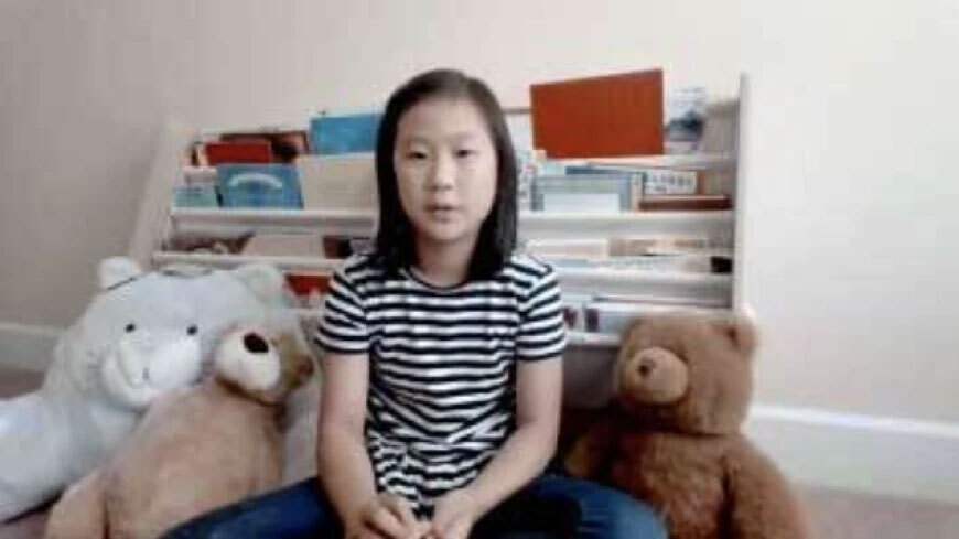 Photograph of a girl sitting on her bed with stuffed animals.