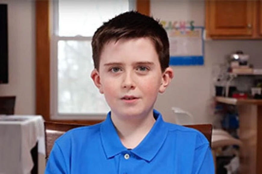 Photograph of a boy sitting in his kitchen.