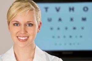 An optometrist smiling in front of an eye chart.