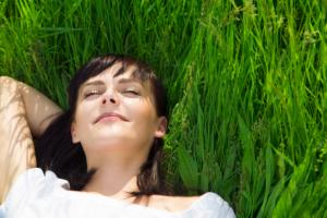 A woman smiling and laying down on a field of grass.