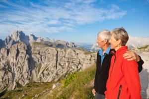 A senior couple hiking outdoors and looking at a view of mountains.