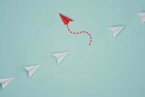 picture of a line of white paper airplanes with one red one flying in the opposite direction