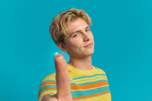young man holding a contact lens on his index finger