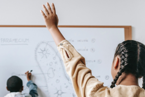 girl looking at white board and raising hand