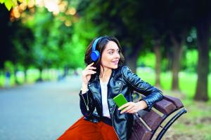 smiling young woman sitting outside on a bench with headphones on