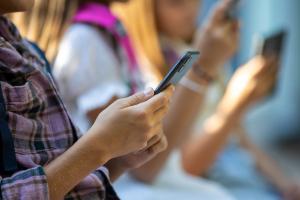 Close-up of boy's hand holding a phone while he sits next to other kids who are also holding their phones