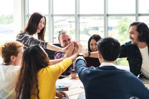 happy group of coworkers sitting around a table with hands in a circle