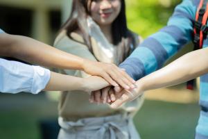 Group of young college students placing hands together