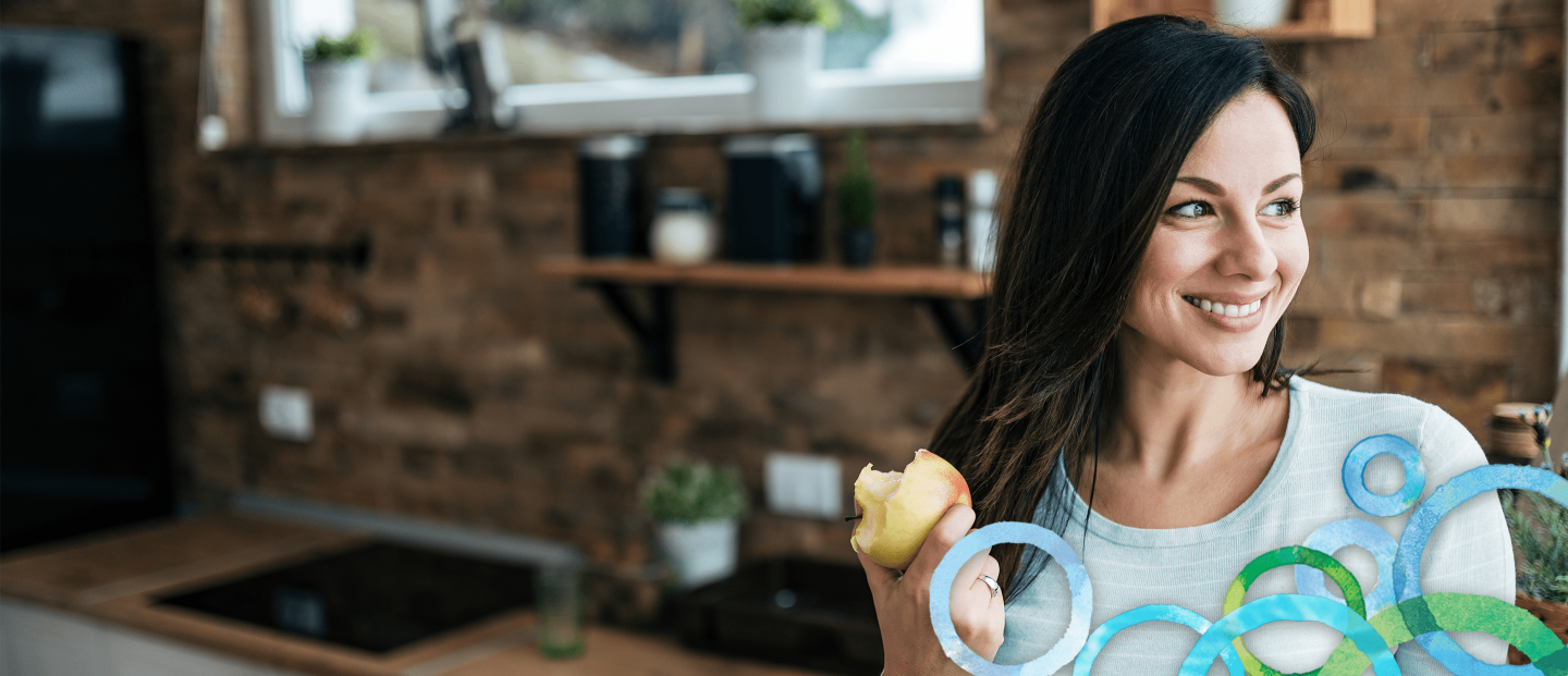 woman smiling and holding an apple in a kitchen