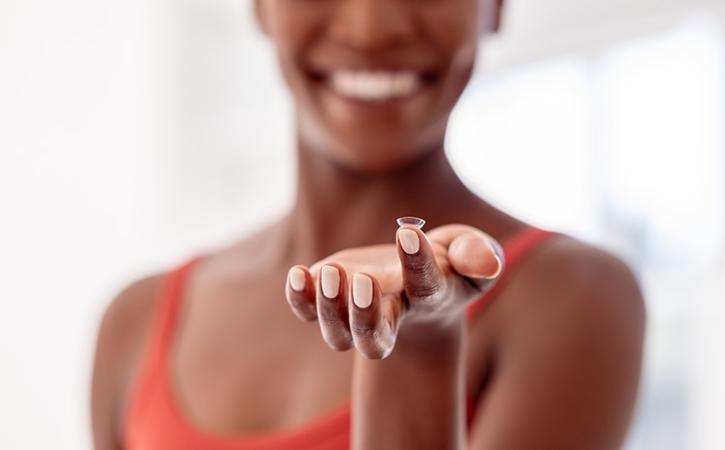 Woman smiling and holding contact lens on index finger.