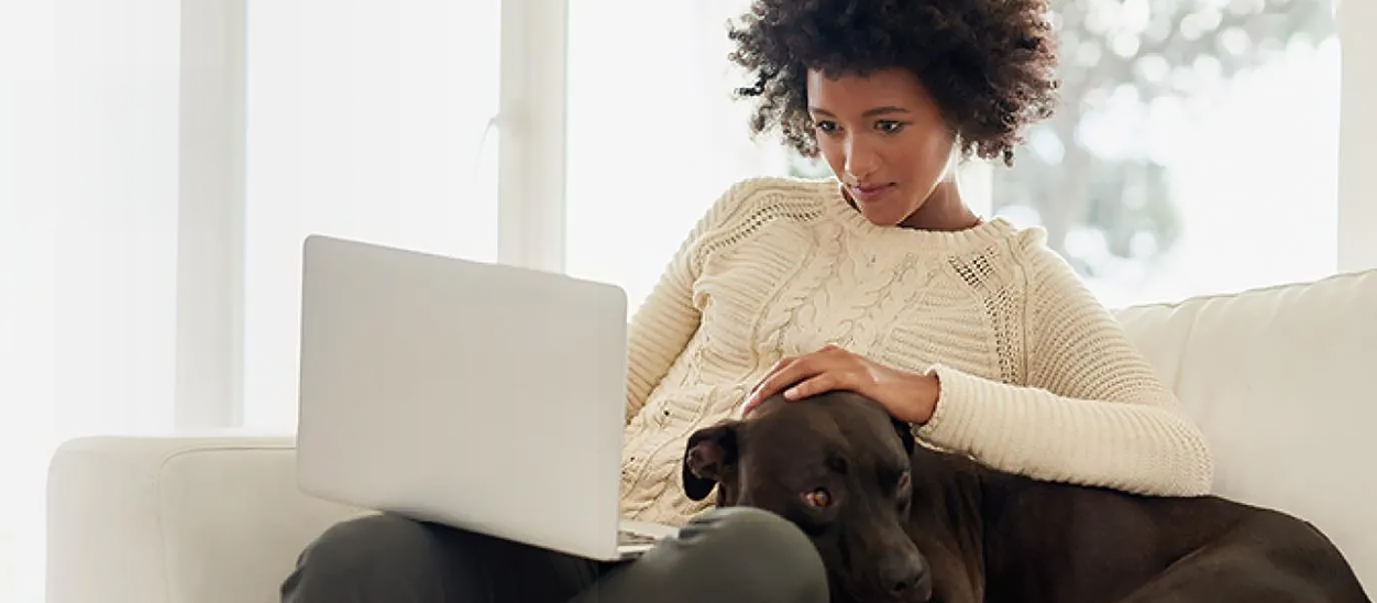 Woman on couch with dog using a laptop