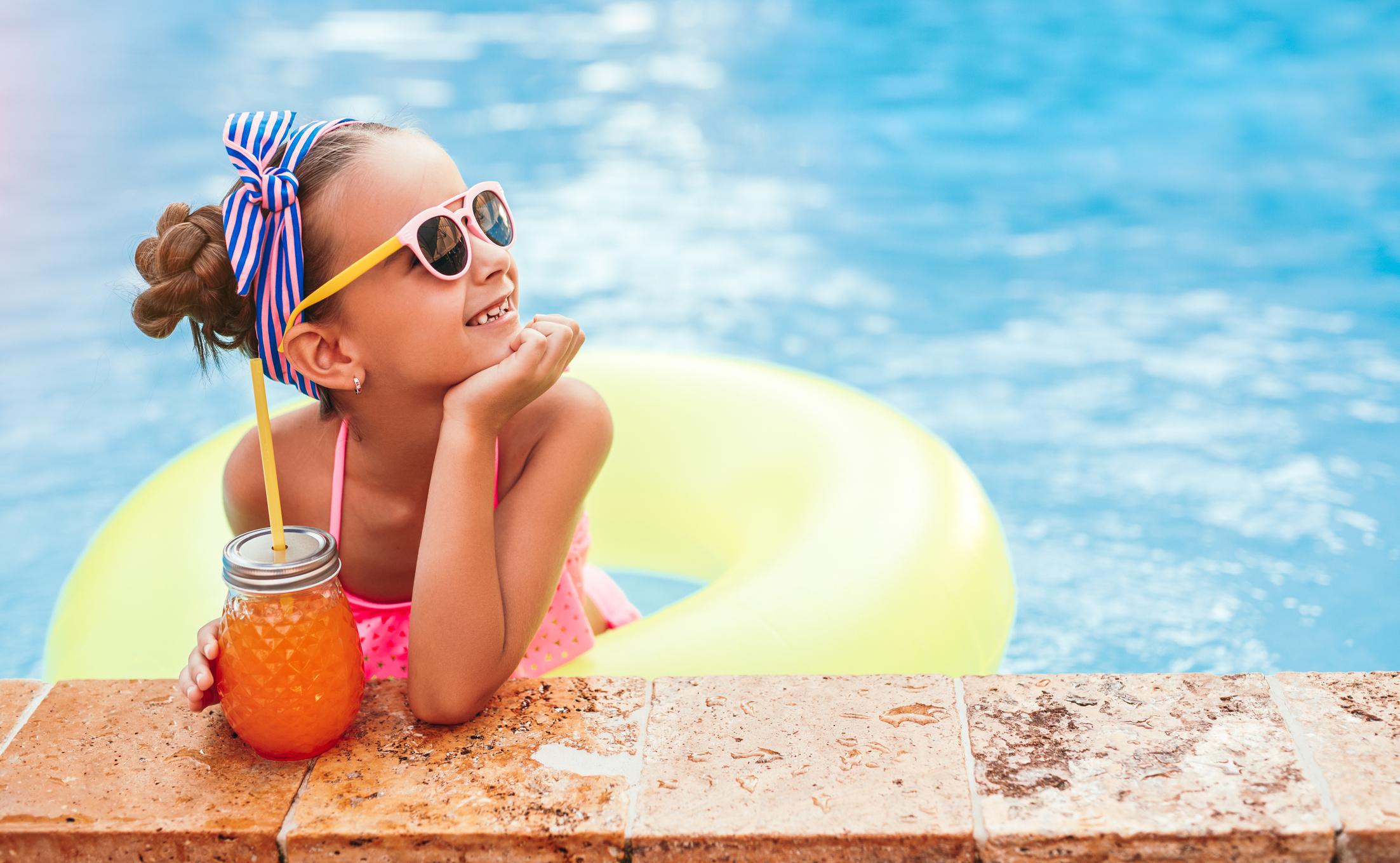 child wearing sunglasses and holding a drink in a swimming pool