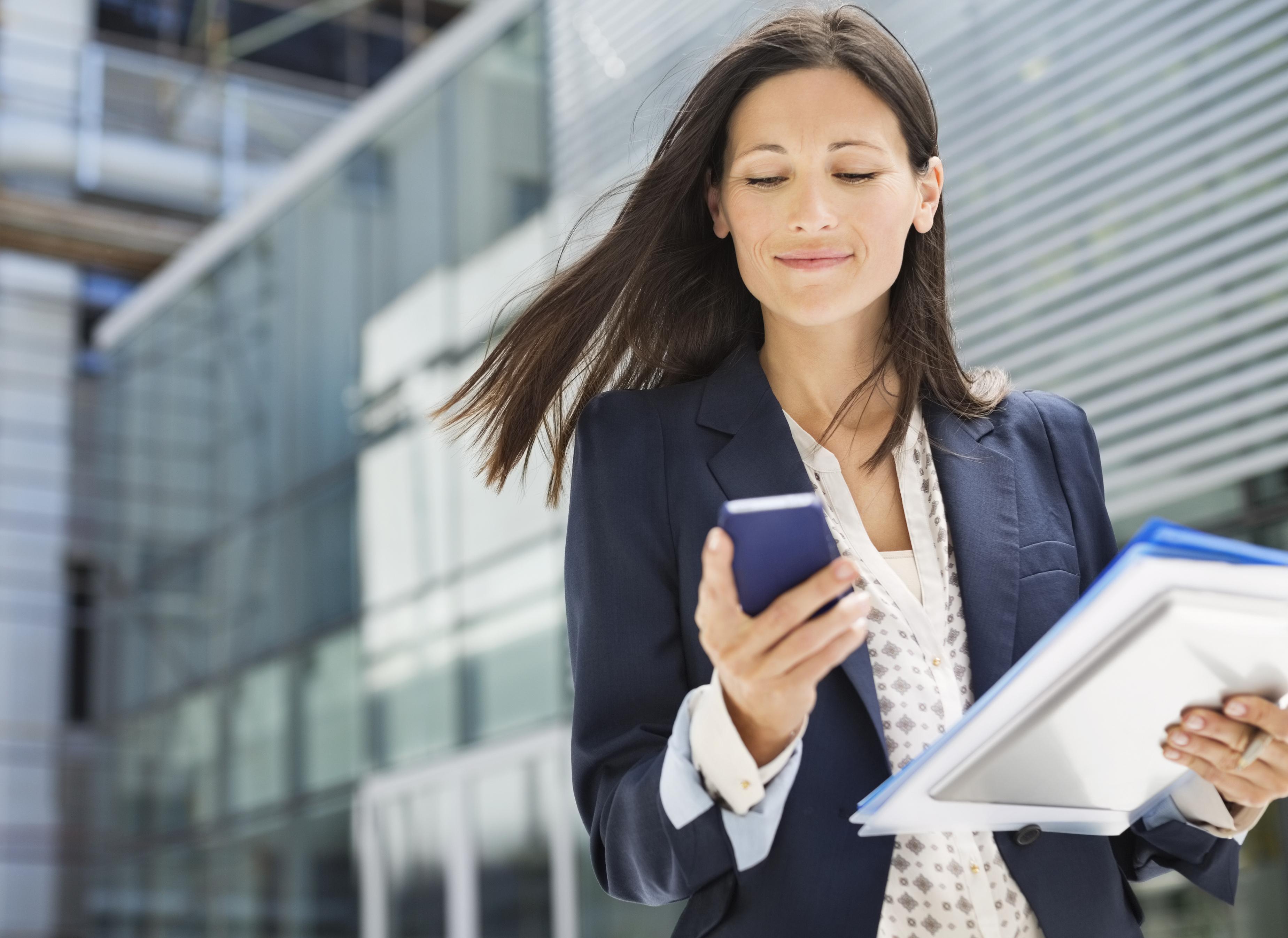 young businesswoman walking outside and looking at her cell phone