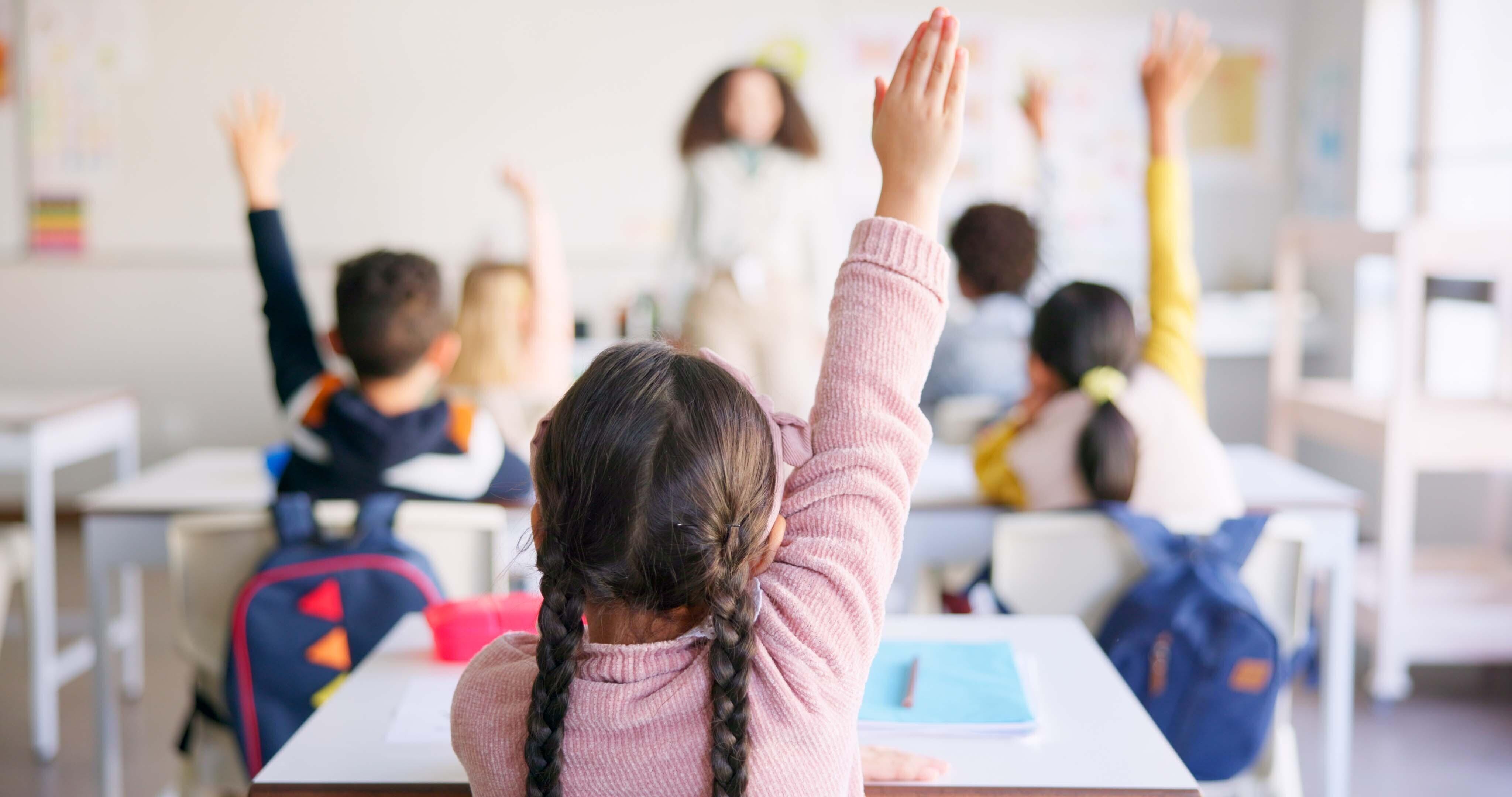 young girl in a classroom with her hand raised.