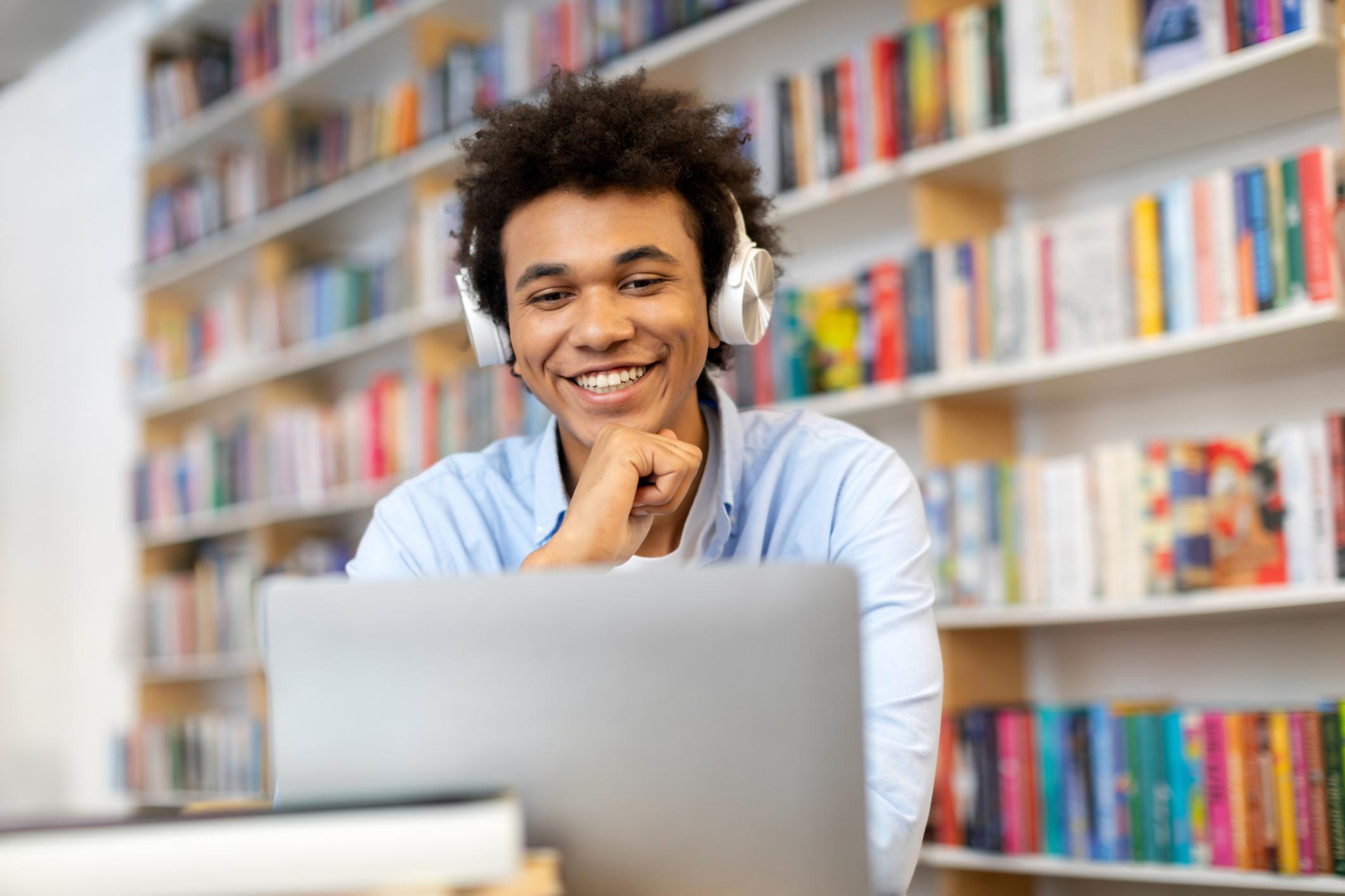a smiling college student in the library and looking at his computer