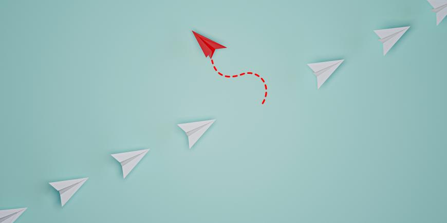 picture of a line of white paper airplanes with one red one flying in the opposite direction