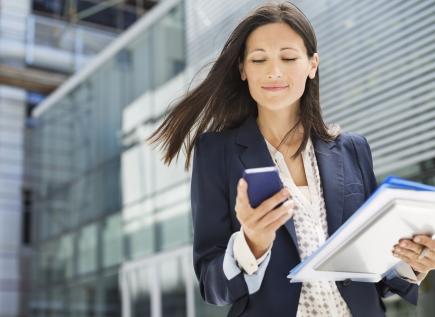 young businesswoman walking outside and looking at her cell phone