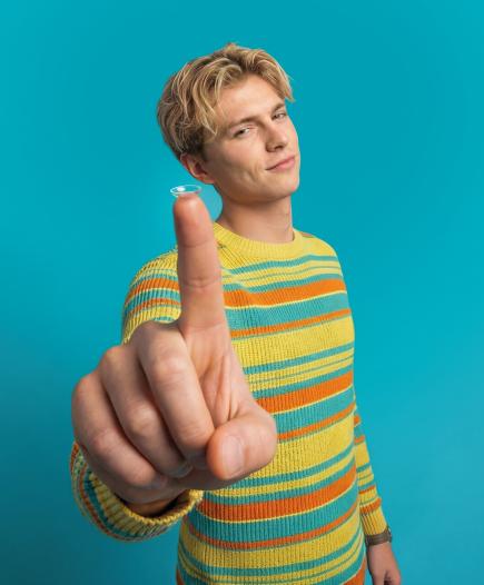 young man holding a contact lens on the tip of his finger