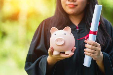 college graduate in cap and gown holding a diploma and a piggy bank