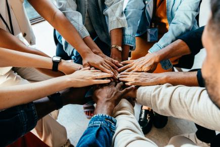 a group of diverse colleagues in a circle collectively holding their hands in the middle