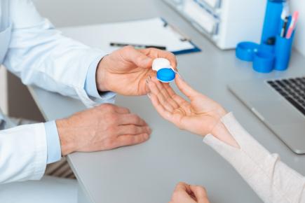 An optometrist handing a patient a contact lens case during an eye exam.