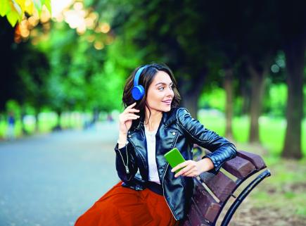 smiling young woman sitting outside on a bench with headphones on