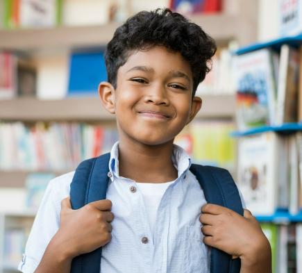 young student smiling and holding a backpack in a library