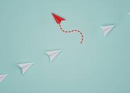 picture of a line of white paper airplanes with one red one flying in the opposite direction