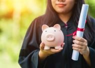 college graduate in cap and gown holding a diploma and a piggy bank