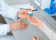 An optometrist handing a patient a contact lens case during an eye exam.