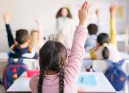 young girl in a classroom with her hand raised.