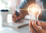 student writing in a notebook and holding lightbulb, indicating learning and new ideas.