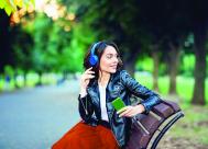 smiling young woman sitting outside on a bench with headphones on