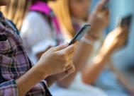 Close-up of boy's hand holding a phone while he sits next to other kids who are also holding their phones