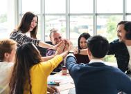 happy group of coworkers sitting around a table with hands in a circle