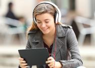 young woman wearing headphones and smiling at a tablet. 